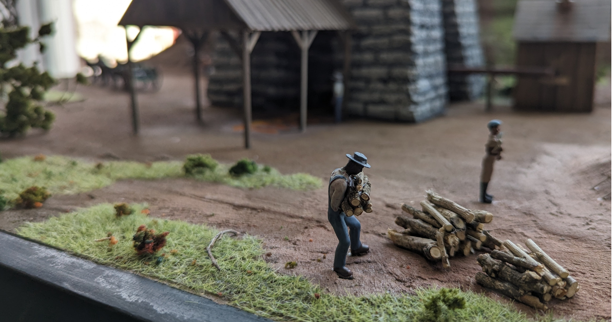 Diorama of an enslaved iron worker carrying wood in front of a furnace